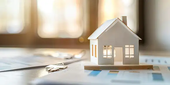 Miniaturhaus auf Dokumenten vor sonnigem Fenster