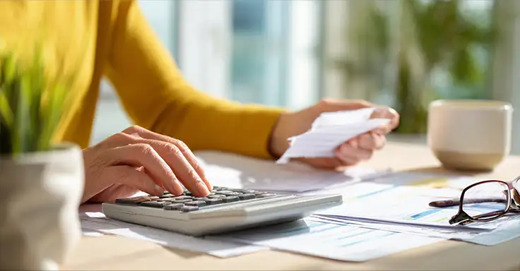 Person mit Taschenrechner und Dokumenten am Tisch