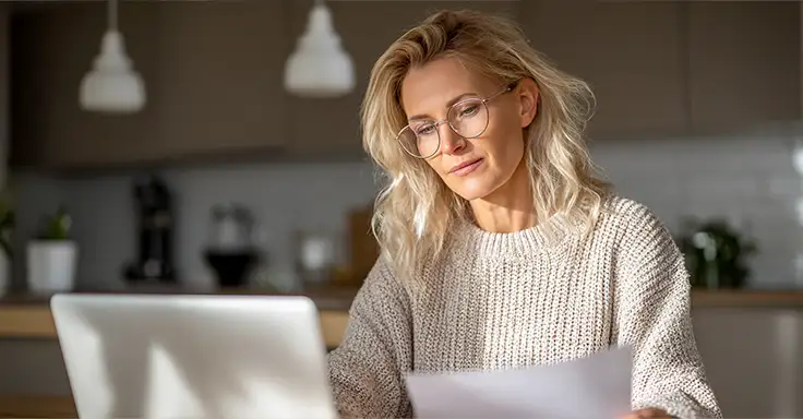 Frau mit Brille liest Dokument am Laptop in moderner Küche